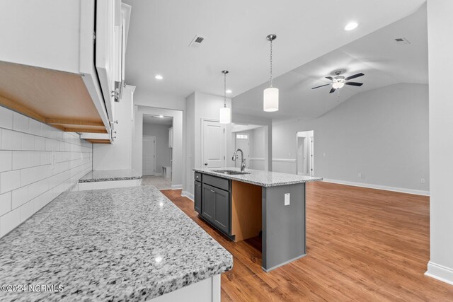 kitchen with sink, light wood-type flooring, ceiling fan, and light stone counters