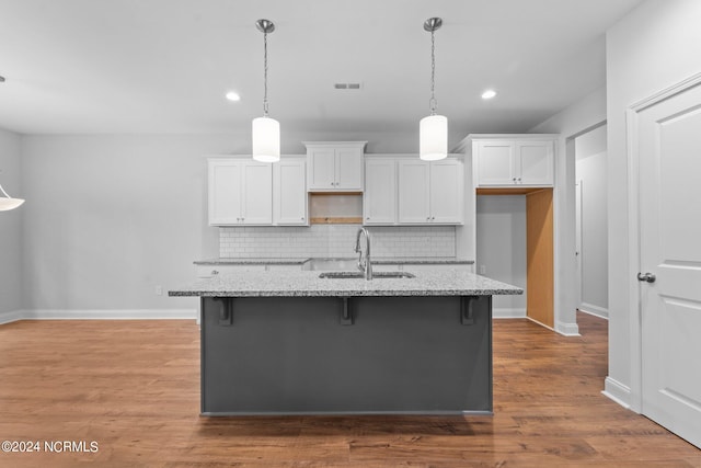 kitchen with sink, backsplash, a kitchen island with sink, light stone countertops, and wood-type flooring