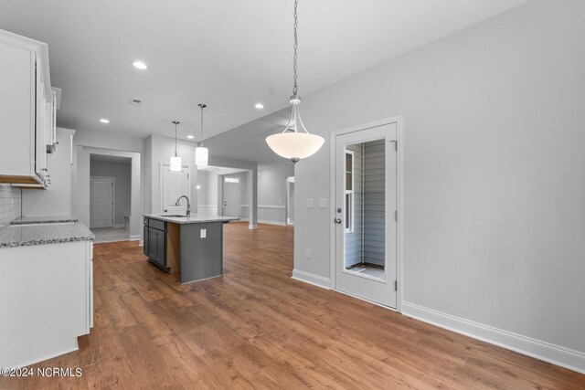 kitchen with a kitchen island with sink, light stone countertops, hanging light fixtures, and hardwood / wood-style floors