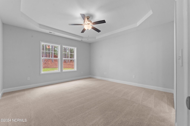 empty room featuring light carpet, baseboards, visible vents, and a tray ceiling