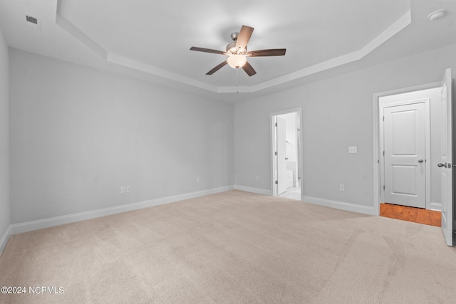 empty room with carpet, a raised ceiling, visible vents, ceiling fan, and baseboards