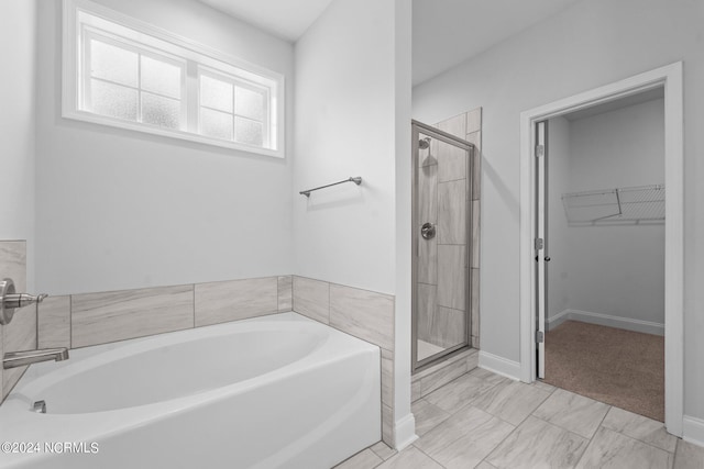 bathroom featuring a spacious closet, a shower stall, a bath, and baseboards