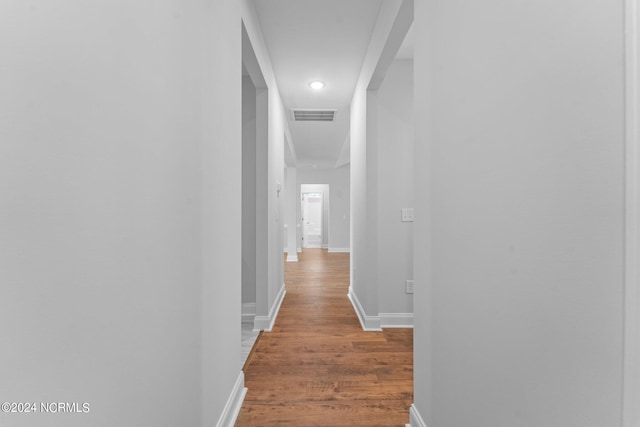 hallway featuring baseboards, visible vents, and wood finished floors