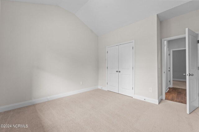 unfurnished bedroom with light carpet, vaulted ceiling, and a closet