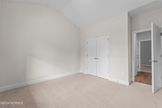 unfurnished bedroom with lofted ceiling, carpet, baseboards, and a closet