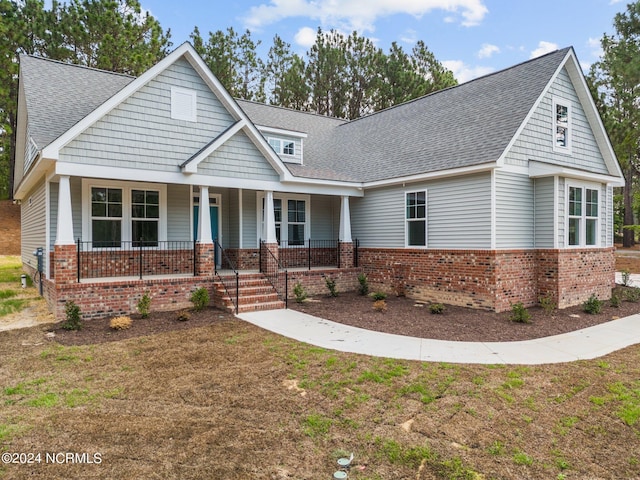 view of front of property with covered porch, roof with shingles, and brick siding