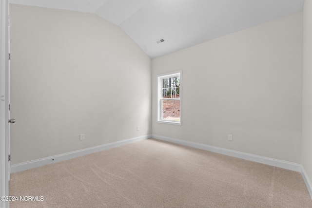 carpeted spare room with baseboards, visible vents, and vaulted ceiling