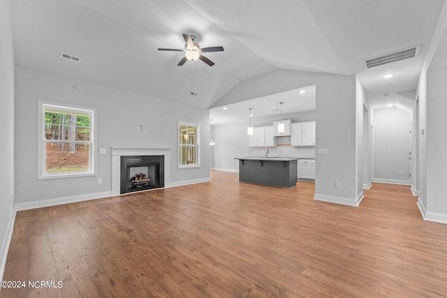 unfurnished living room with vaulted ceiling, sink, ceiling fan, and light hardwood / wood-style floors