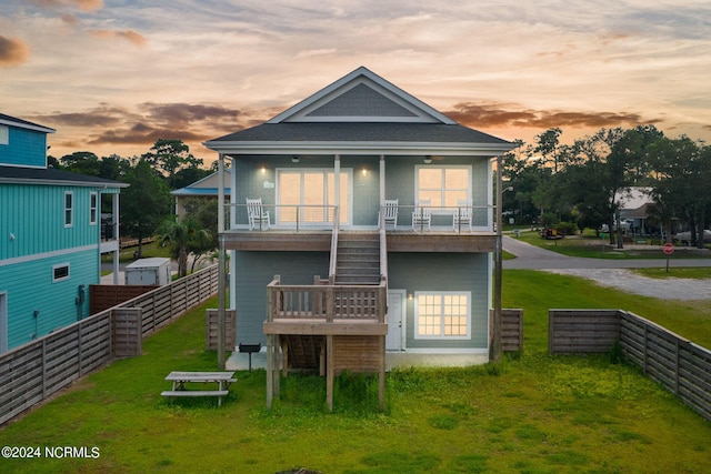 back house at dusk featuring a balcony and a lawn