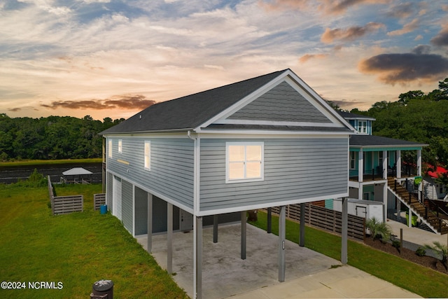 back house at dusk with a carport and a lawn