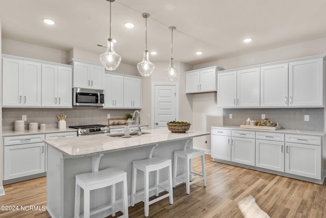 kitchen featuring stainless steel microwave, hanging light fixtures, white cabinets, a sink, and range