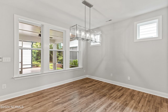 unfurnished dining area with hardwood / wood-style flooring, ceiling fan with notable chandelier, and a wealth of natural light