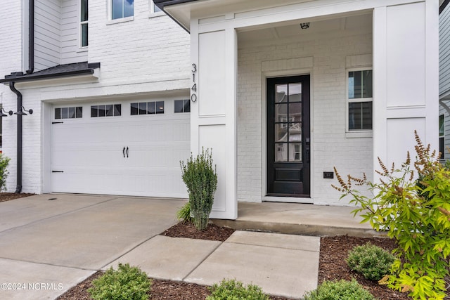 doorway to property with a garage, concrete driveway, and brick siding