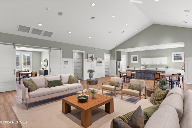 living room featuring high vaulted ceiling, light hardwood / wood-style flooring, and a barn door