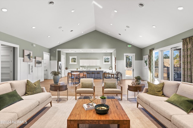 living room with sink, light wood-type flooring, and high vaulted ceiling