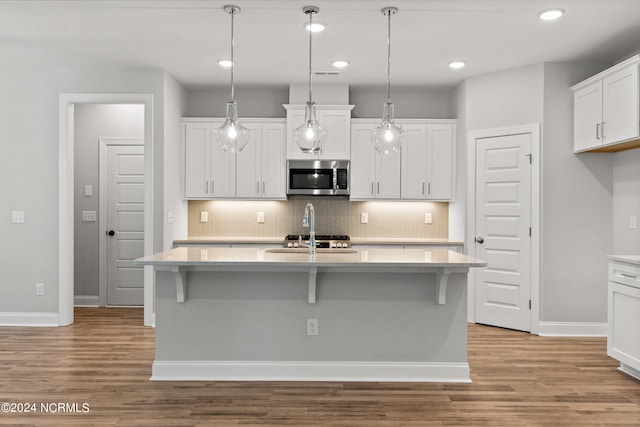 kitchen with white cabinetry, backsplash, a center island with sink, and light wood-type flooring