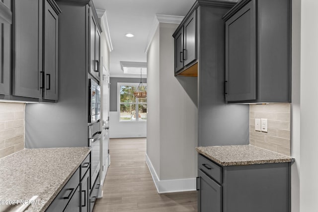 kitchen with light stone countertops, light wood-type flooring, backsplash, crown molding, and gray cabinets