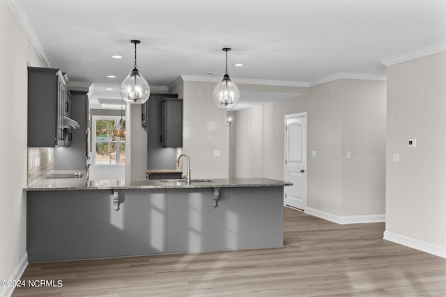 kitchen featuring pendant lighting, light stone countertops, kitchen peninsula, and sink