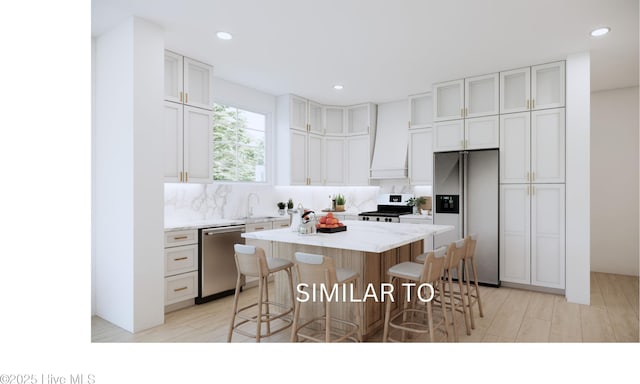 kitchen with a kitchen island, appliances with stainless steel finishes, a kitchen breakfast bar, light wood-style floors, and a sink