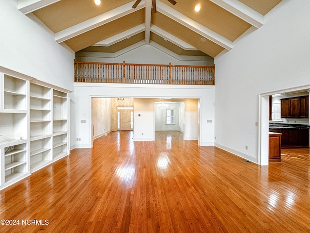 unfurnished living room with high vaulted ceiling, beamed ceiling, light hardwood / wood-style floors, and ceiling fan