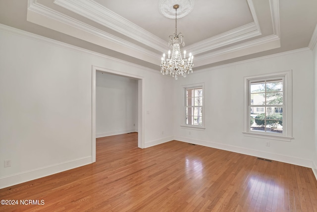 unfurnished room featuring a chandelier, light hardwood / wood-style floors, crown molding, and a tray ceiling