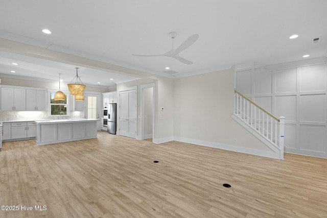 unfurnished living room with ceiling fan, light hardwood / wood-style flooring, sink, and ornamental molding