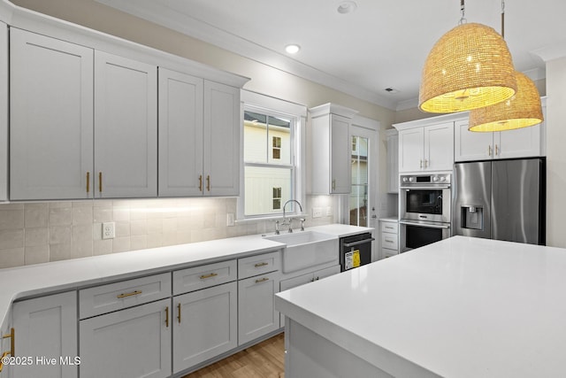 kitchen featuring sink, light wood-type flooring, appliances with stainless steel finishes, tasteful backsplash, and decorative light fixtures