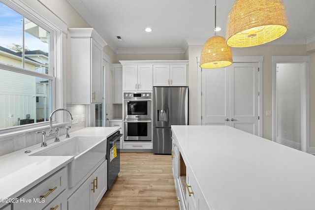 kitchen with appliances with stainless steel finishes, light wood-type flooring, sink, white cabinets, and hanging light fixtures