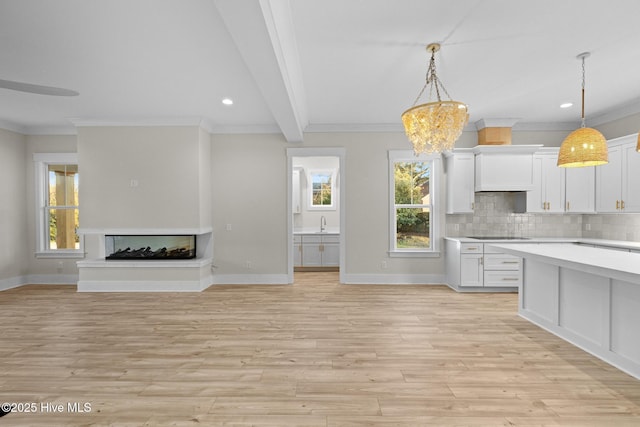 kitchen with a multi sided fireplace, decorative light fixtures, white cabinetry, and crown molding