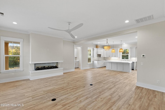 unfurnished living room featuring light wood-type flooring, crown molding, ceiling fan, and a healthy amount of sunlight