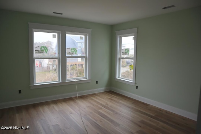 spare room featuring visible vents, baseboards, and wood finished floors