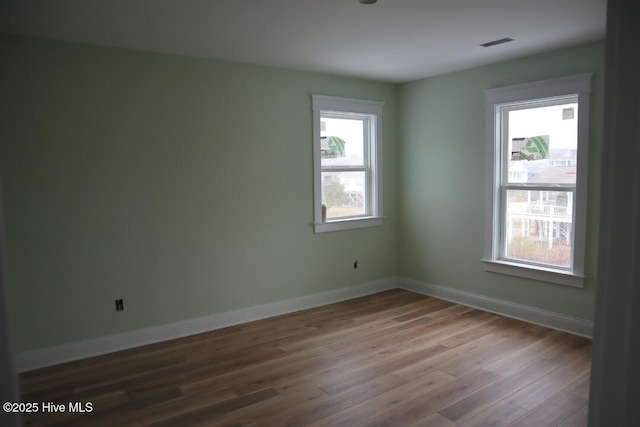 empty room featuring visible vents, wood finished floors, and baseboards