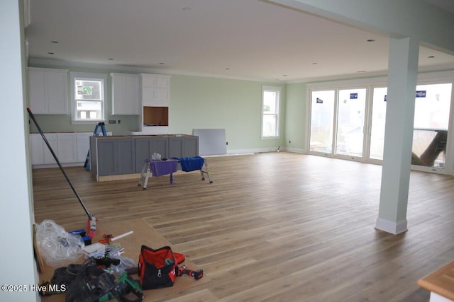 interior space featuring baseboards, a kitchen island, ornamental molding, white cabinets, and light wood-type flooring