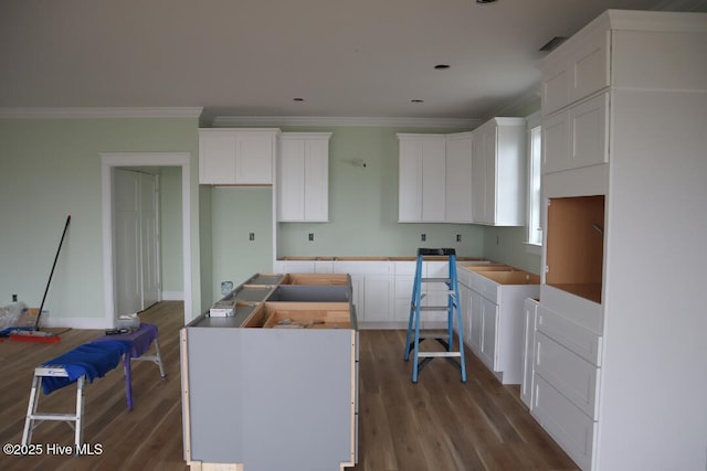 kitchen with a kitchen island, wood finished floors, crown molding, and white cabinetry