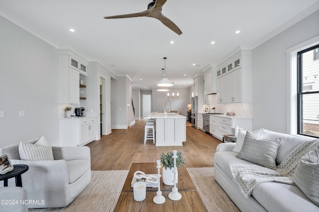 living room featuring light hardwood / wood-style floors, ceiling fan, ornamental molding, and sink