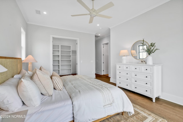 bedroom with light wood-type flooring, a walk in closet, ceiling fan, crown molding, and a closet