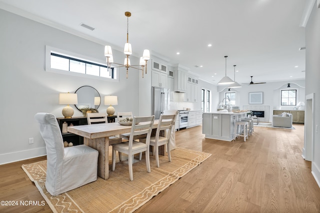 dining area with ceiling fan with notable chandelier, a healthy amount of sunlight, sink, and light hardwood / wood-style flooring