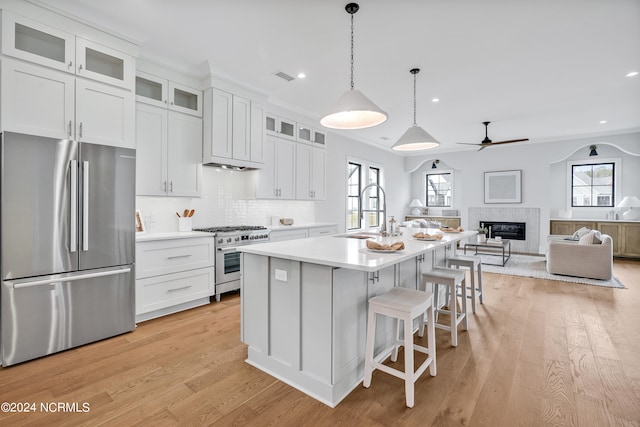 kitchen with sink, appliances with stainless steel finishes, an island with sink, white cabinets, and light wood-type flooring