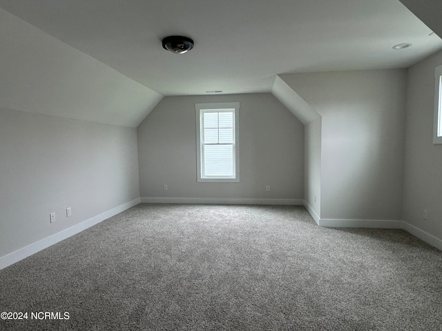 additional living space featuring vaulted ceiling and carpet flooring