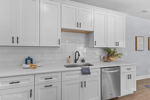 kitchen with light wood-type flooring, backsplash, stainless steel dishwasher, sink, and white cabinets