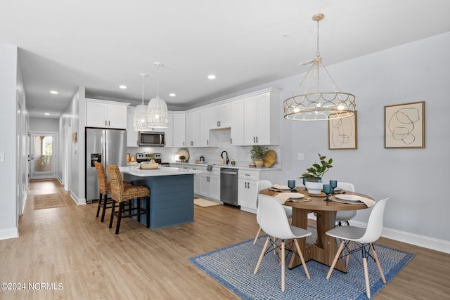 kitchen with white cabinetry, light wood-type flooring, decorative light fixtures, and appliances with stainless steel finishes