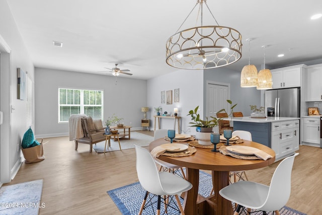 dining space with ceiling fan with notable chandelier and light hardwood / wood-style floors