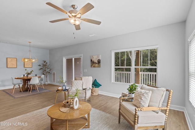 living room with ceiling fan with notable chandelier and light hardwood / wood-style flooring