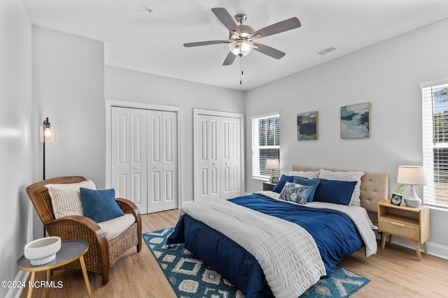 bedroom featuring ceiling fan, light hardwood / wood-style floors, and two closets