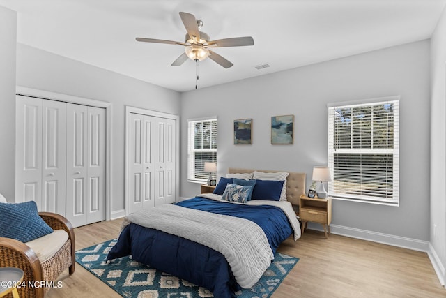 bedroom with two closets, light hardwood / wood-style flooring, and ceiling fan