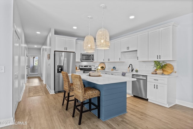 kitchen with light wood-type flooring, stainless steel appliances, white cabinets, a kitchen island, and hanging light fixtures