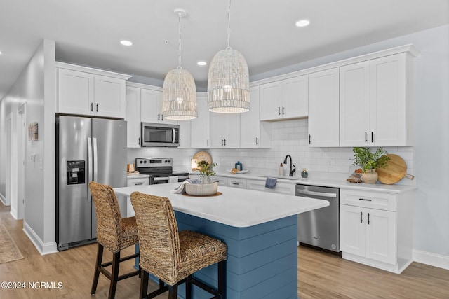 kitchen with a center island, backsplash, appliances with stainless steel finishes, white cabinets, and light wood-type flooring