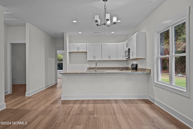 kitchen with light wood-type flooring, black stove, white cabinetry, pendant lighting, and light stone counters