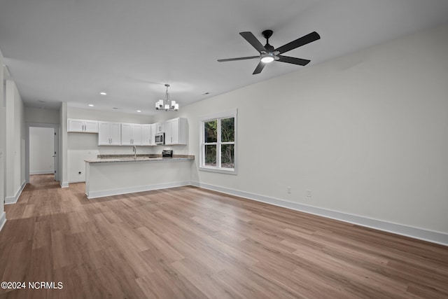 unfurnished living room featuring sink, light hardwood / wood-style flooring, and ceiling fan with notable chandelier