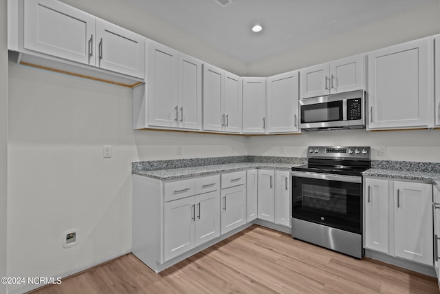 kitchen with white cabinetry, light stone counters, stainless steel appliances, and light wood-type flooring